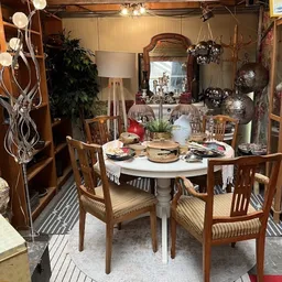 Ingerichte eethoek met ronde tafel, houten stoelen en diverse decoratie-items in een kringloopwinkel