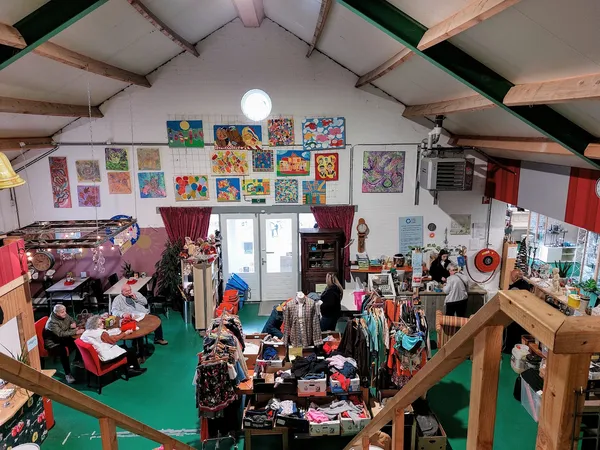 Overzicht van de winkelvloer met rekken kleding, kunstwerken aan de muur en diverse tweedehandsartikelen