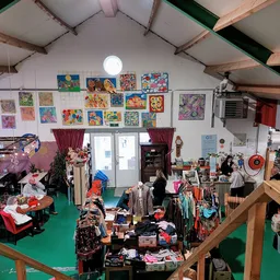 Overzicht van de winkelvloer met rekken kleding, kunstwerken aan de muur en diverse tweedehandsartikelen