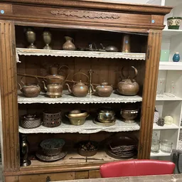 Houten vitrinekast met vier schappen vol koperen en metalen serviesgoed, pannen en decoratieve items