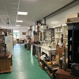 Binnenkant van kringloopwinkel met diverse meubels, kastjes en decoratieve voorwerpen langs beide zijden