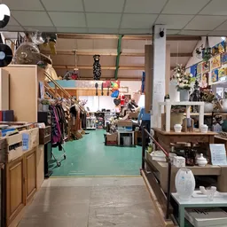 Winkelvloer van kringloopcentrum met groene vloer, kledingrekken, kasten, decoratie en verschillende afdelingen zichtbaar