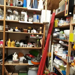 Houten stellingen met huishoudelijke spullen, servies, kannen en diverse tweede-handse artikelen