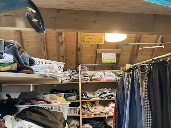 Houten stellingen met tweedehands kleding, linnengoed en overige textiel in een kringloopwinkel