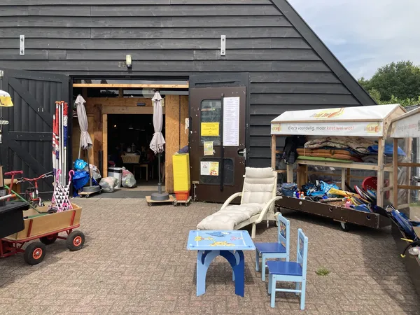 Zwarte gevel van kringloopwinkel met open deuren, daarvoor speelgoed en gebruiksartikelen op het erf