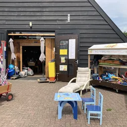 Zwarte gevel van kringloopwinkel met open deuren, daarvoor speelgoed en gebruiksartikelen op het erf