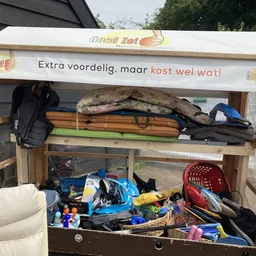 Overvolle uitstalkast met diverse tweedehands spullen en huishoudartikelen op meerdere niveaus