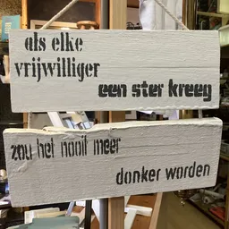 Twee houten borden met Nederlandse tekst over vrijwilligers en donaties