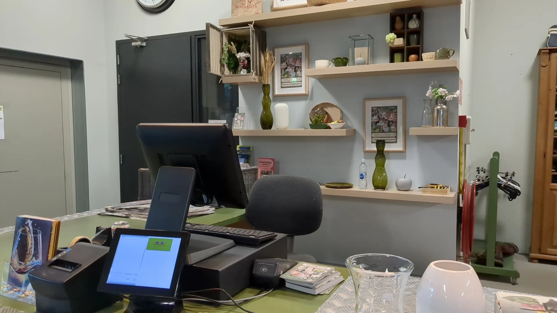 Kantoorruimte met bureau, computer, zwarte bureaustoel en grijze muur met houten wandplanken met decoratie