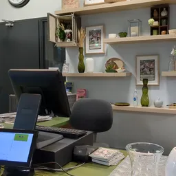 Kantoorruimte met bureau, computer, zwarte bureaustoel en grijze muur met houten wandplanken met decoratie