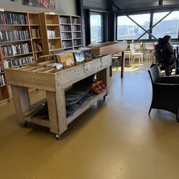 Winkelvloer met houten toonbank, boekenkasten, zithoeken en grote ramen met uitzicht op de stad
