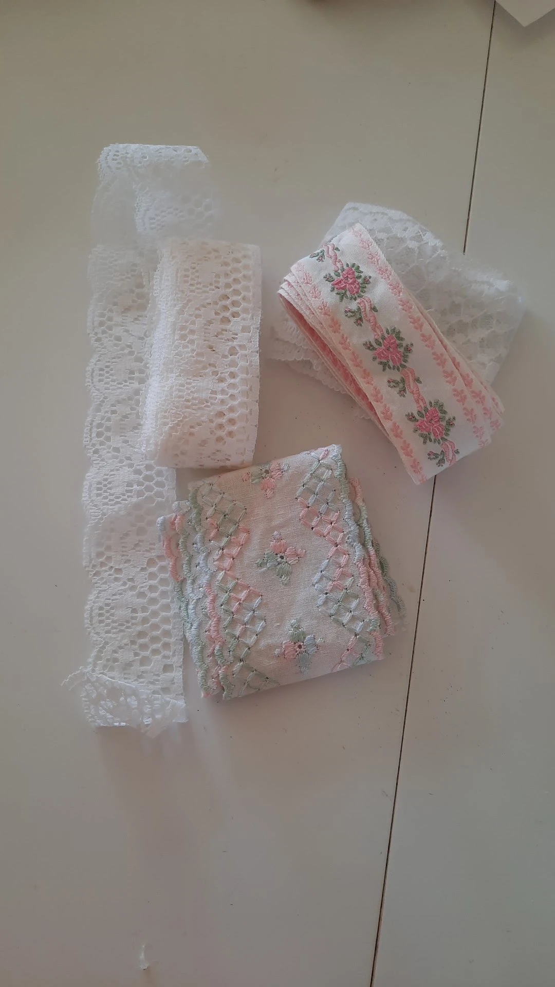 Drie verschillende kant- en textielstukken met bloemmotieven en kantwerk in wit en roze tinten