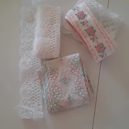 Drie verschillende kant- en textielstukken met bloemmotieven en kantwerk in wit en roze tinten