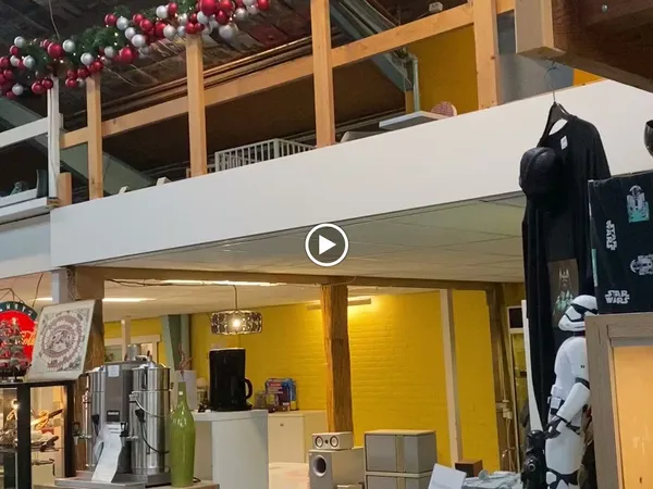 Winkelinterieur met gele wand, witte afdakking, en uitstallingen met kleding en merchandise
