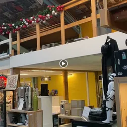 Winkelinterieur met gele wand, witte afdakking, en uitstallingen met kleding en merchandise