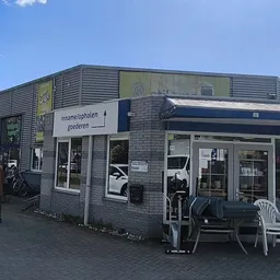 Voorgevel van kringloopwinkel met ingang, ramen en witte stoelen op het terras