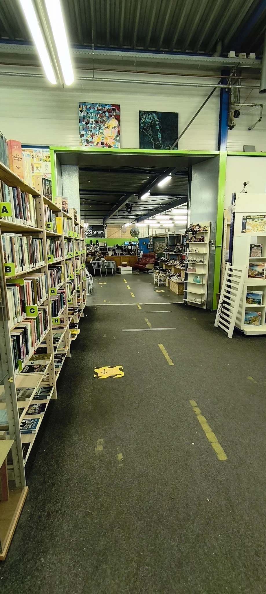 Winkelvloer met boekenrekken links, diverse spullen en meubels, gele markeringen op de grond