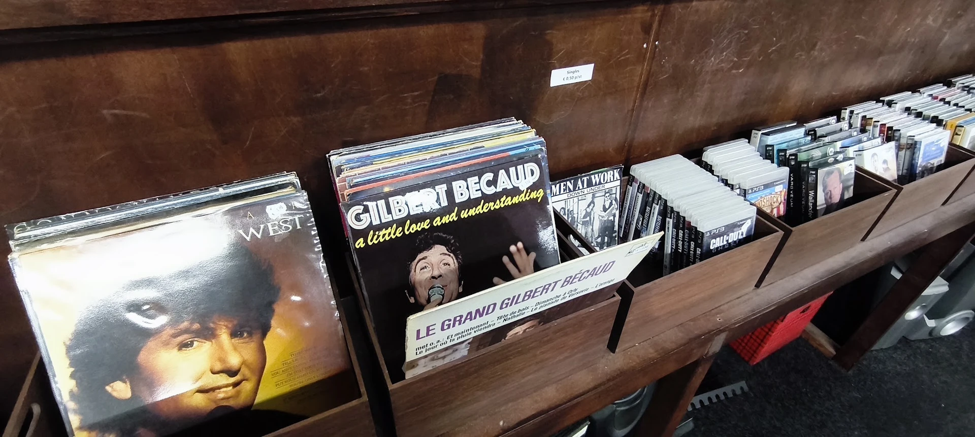 Rekken met tweedehands cd's en dvd's, waaronder een duidelijk zichtbare Gilbert Bécaud-album op de voorgrond