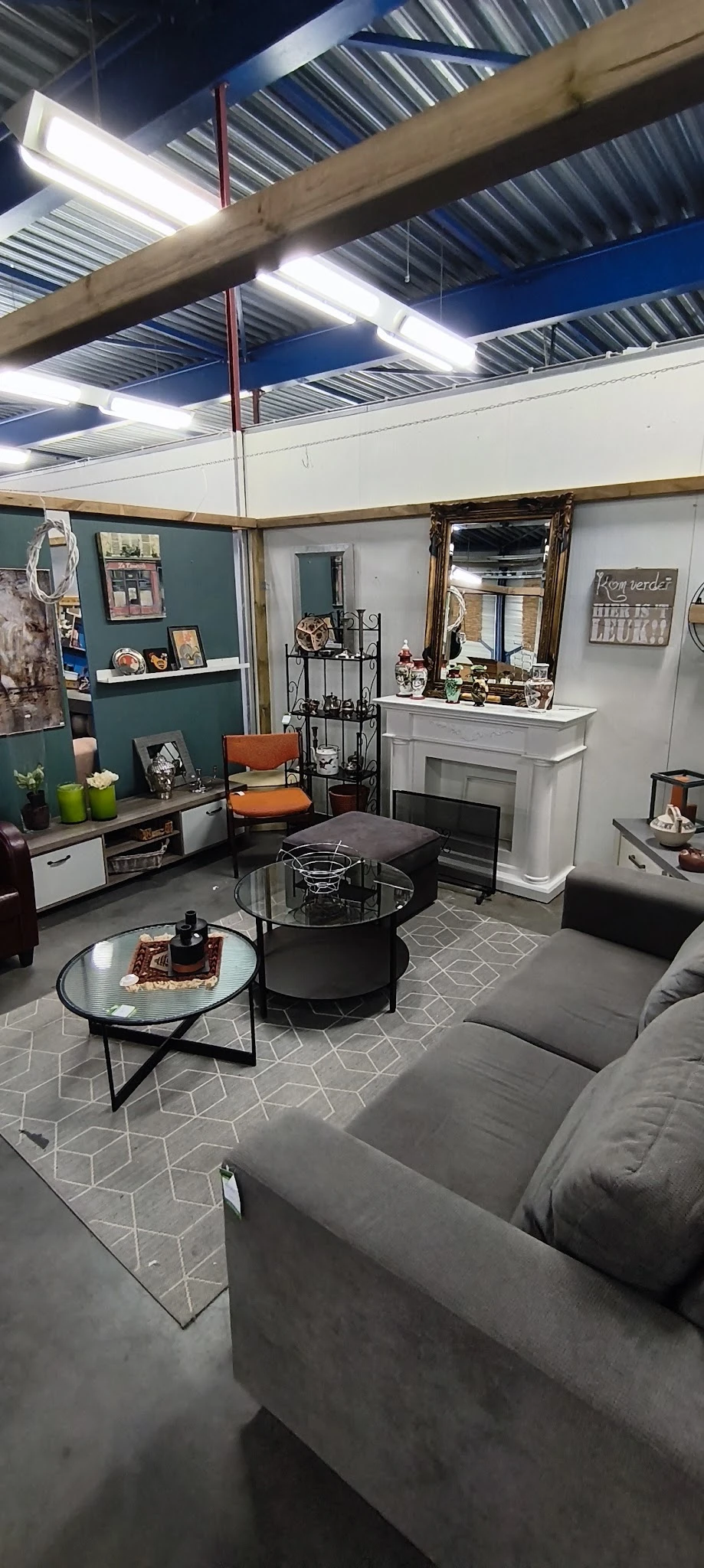 Woonkamer inrichting met meubels: grijze bank, zwarte salontafel, orangegrijze fauteuil, kast met spiegels en decoratie.