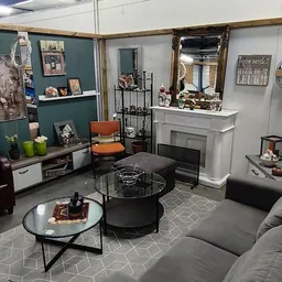 Woonkamer inrichting met meubels: grijze bank, zwarte salontafel, orangegrijze fauteuil, kast met spiegels en decoratie.