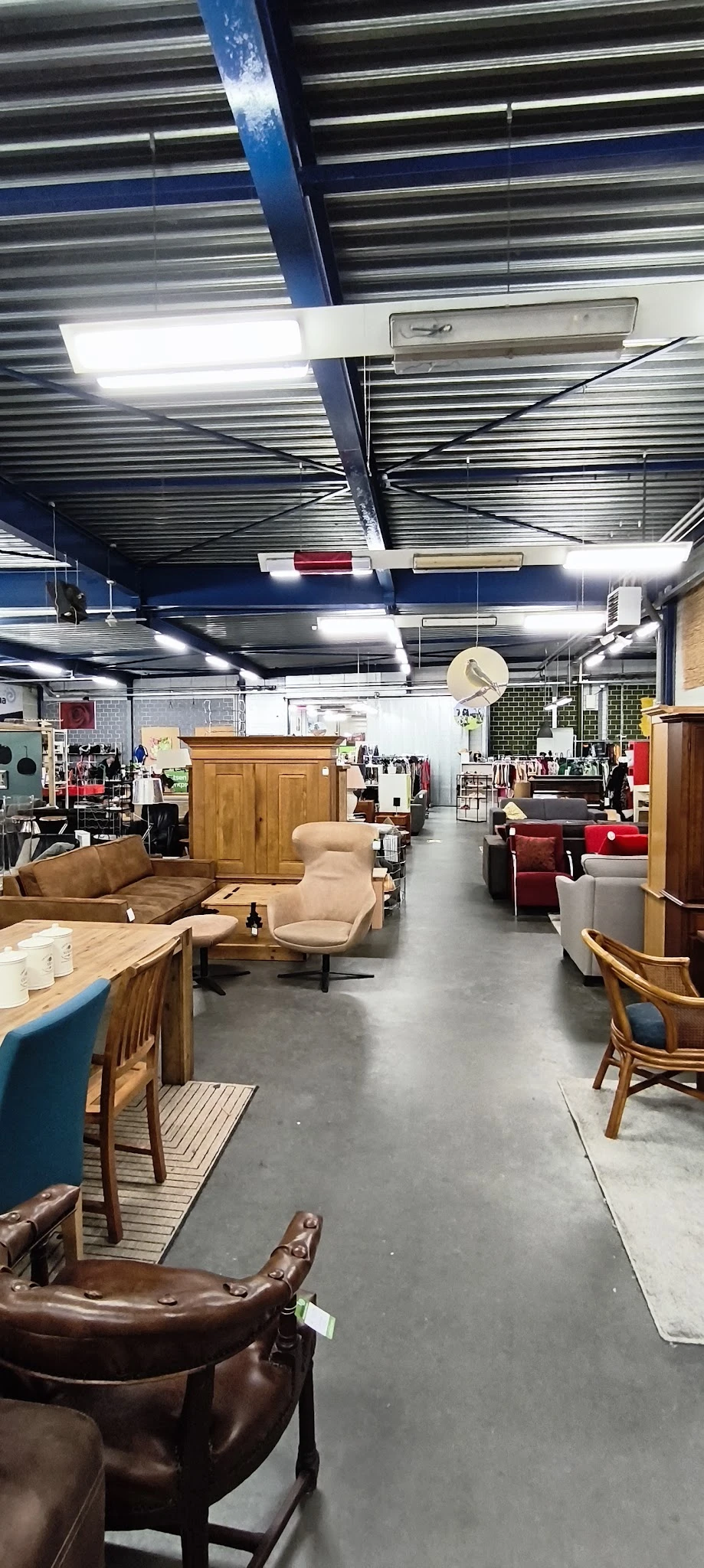 Winkelvloer met meubels: bruine leren bank, beige fauteuil, houten kasten en diverse zitmeubels op grijs beton
