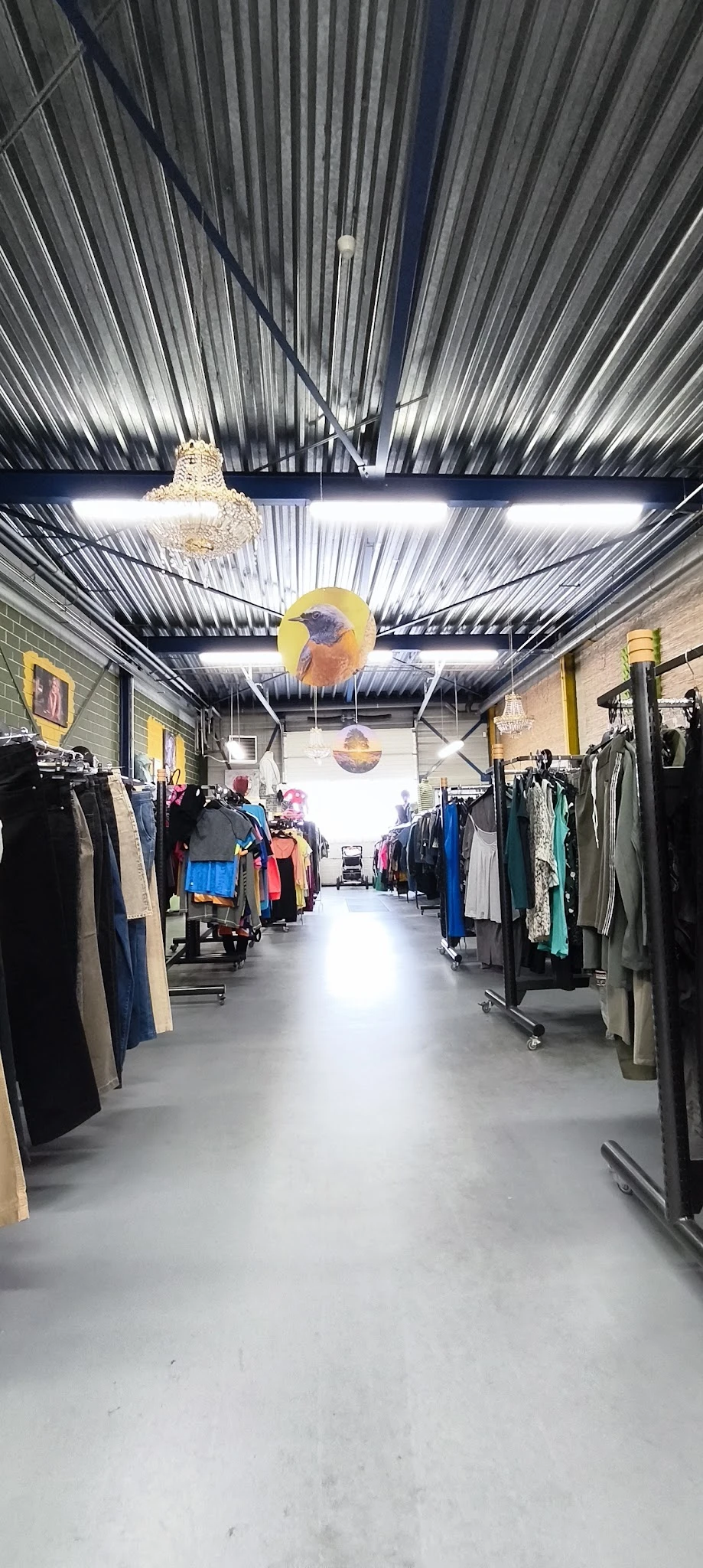 Winkelvloer van kringloopwinkel met rekken tweedehands kleding aan beide zijden en gele decoratie aan het plafond