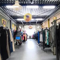 Winkelvloer van kringloopwinkel met rekken tweedehands kleding aan beide zijden en gele decoratie aan het plafond