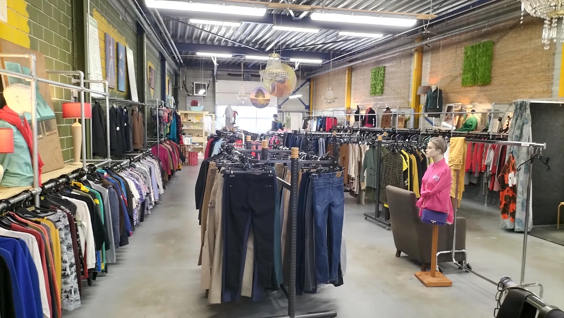 Winkelvloer met kledingrekken vol tweedehands kleding, tassen en accessoires onder fluorescente verlichting