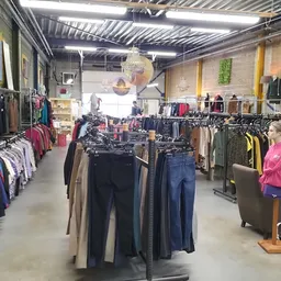 Winkelvloer met kledingrekken vol tweedehands kleding, tassen en accessoires onder fluorescente verlichting