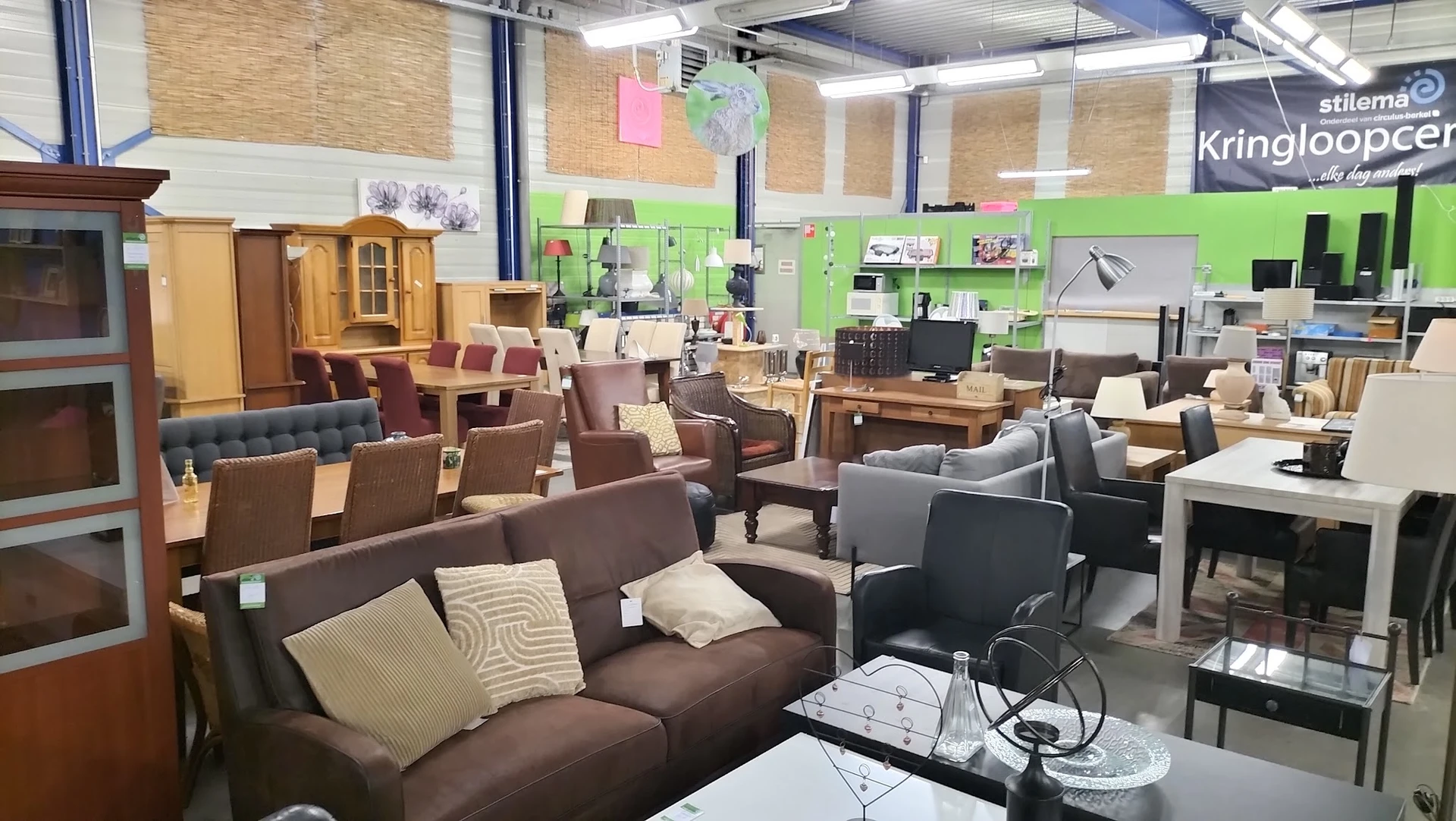 Winkelvloer met bruine en grijze fauteuils en zitmeubels, groene wand op achtergrond, diverse meubels en huishoudartikelen
