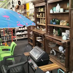Winkelbinnenruimte met houten stellingkasten vol huishoudwaar, groene stoelen en blauwe parasol