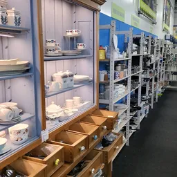 Vitrinekast met servies en kopjes, rechts stellingen met huishoudartikelen