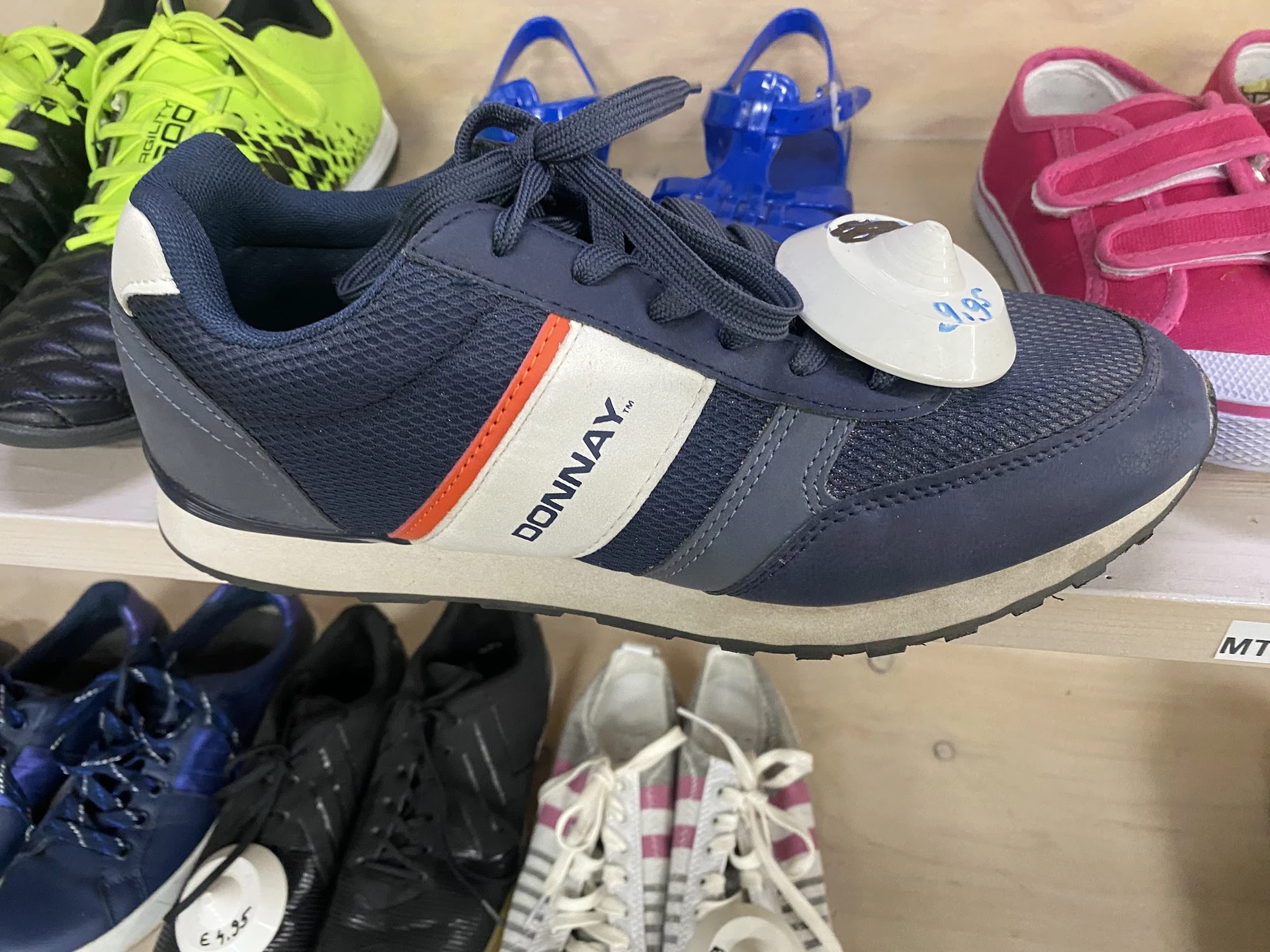 Uitgestalde kinderschoenen op een plank, waaronder een marine-witte sneaker met oranje accent op de voorgrond