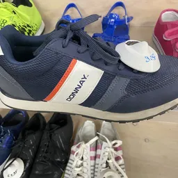 Uitgestalde kinderschoenen op een plank, waaronder een marine-witte sneaker met oranje accent op de voorgrond