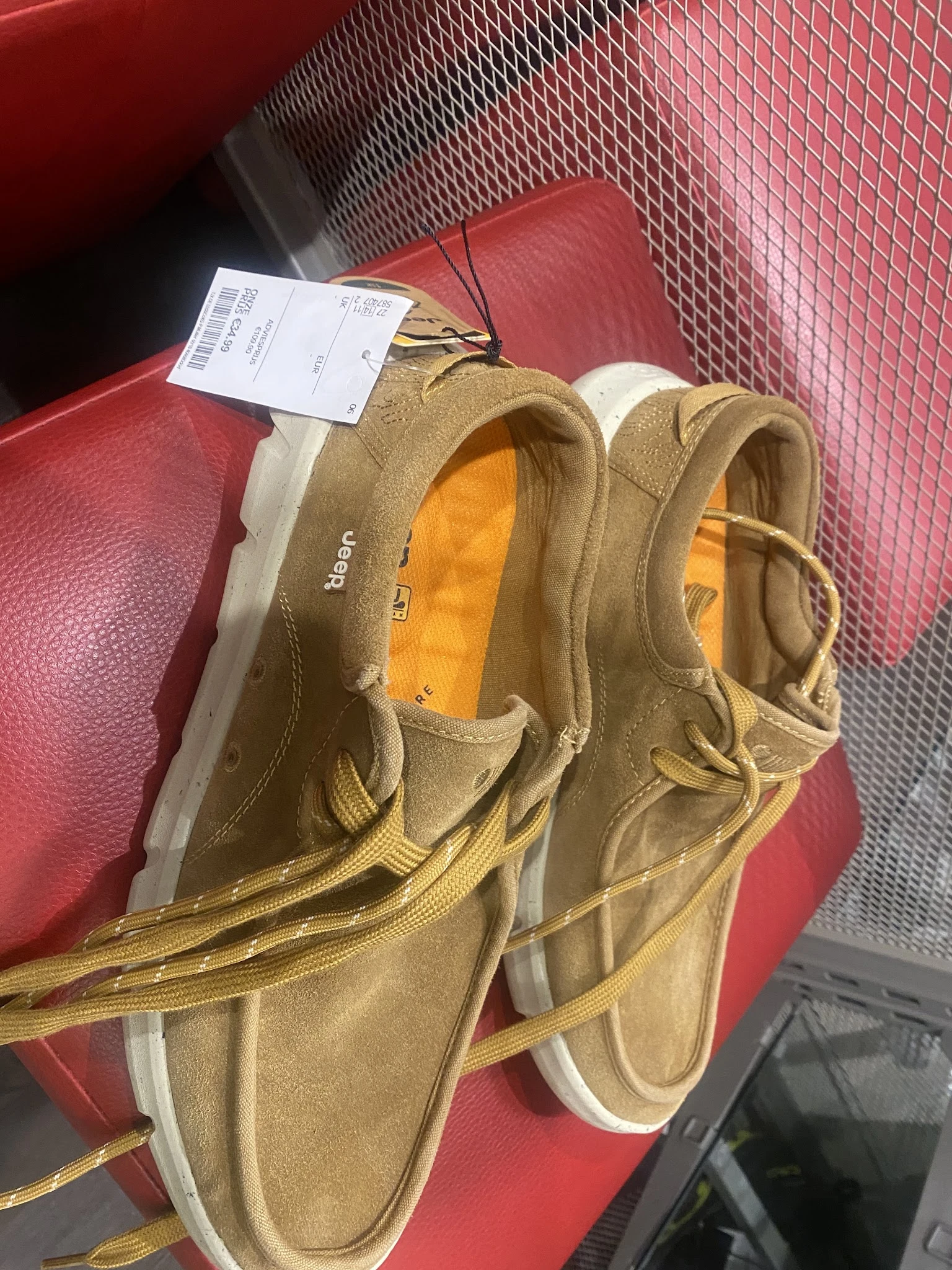 Close-up van een paar beige/tan werkschoenen of laarzen met gele stiksels en oranje voering, met prijskaartje eraan