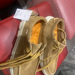 Close-up van een paar beige/tan werkschoenen of laarzen met gele stiksels en oranje voering, met prijskaartje eraan
