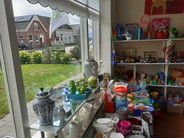 Vensterbank en rekken met diverse tweede-handse artikelen, servies en speelgoed in kringloopwinkel