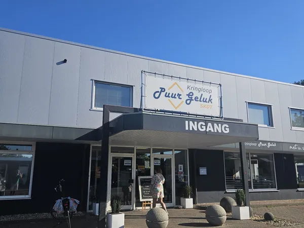 Voorkant van kringloopwinkel Puur Geluk met witte gevel, entree, zwarte luifel en naam duidelijk zichtbaar