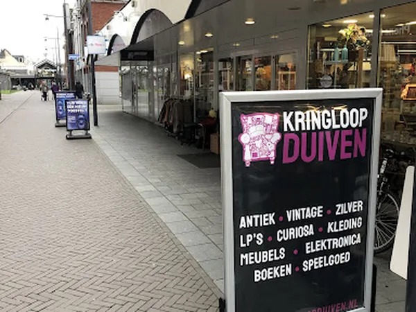 Winkelstraat met etalage van Kringloop Duiven met zwart informatiebord over assortiment