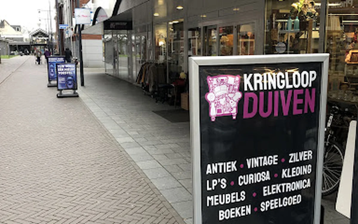 Winkelstraat met etalage van Kringloop Duiven met zwart informatiebord over assortiment