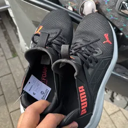 Close-up van een paar zwarte sportschoenen met rode accenten en een wit prijskaartje