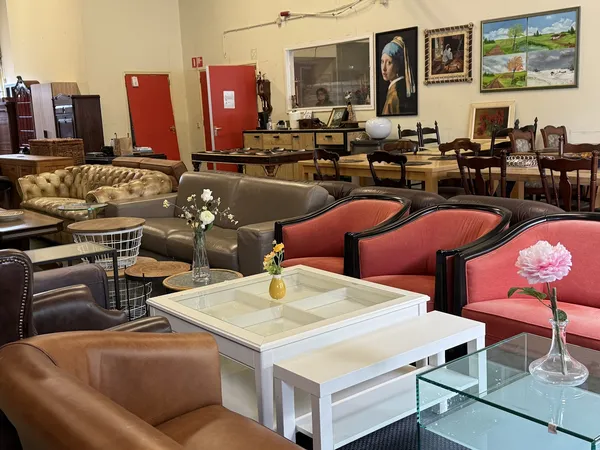 Showroom met diverse meubels: rode stoelen, bruine leren fauteuil, grijze chesterfield bank en witte salontafel met bloemen