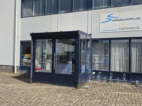 Donkerblauwe entree van kringloopwinkel aan pand met witte gevel en logo