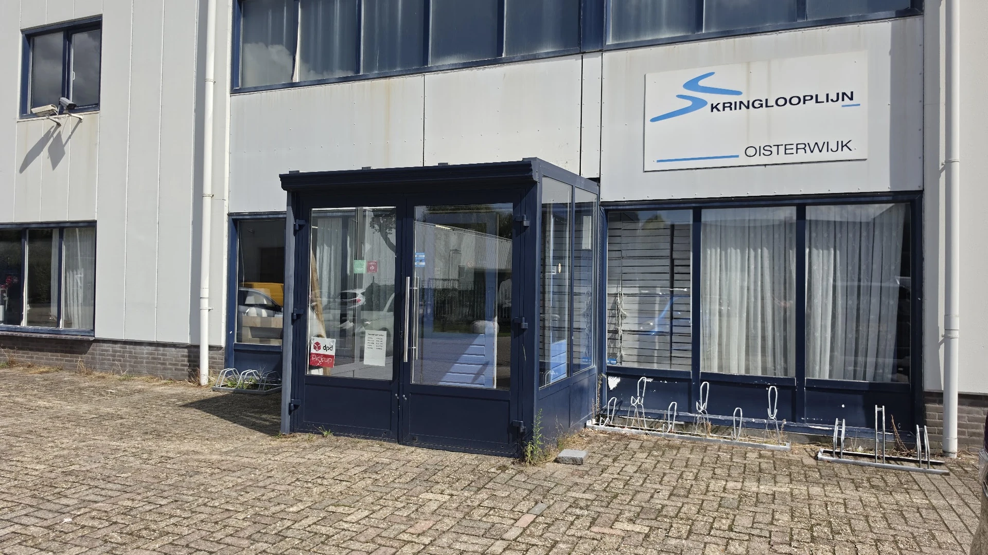 Donkerblauwe entree van kringloopwinkel aan pand met witte gevel en logo