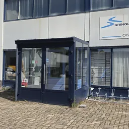 Donkerblauwe entree van kringloopwinkel aan pand met witte gevel en logo