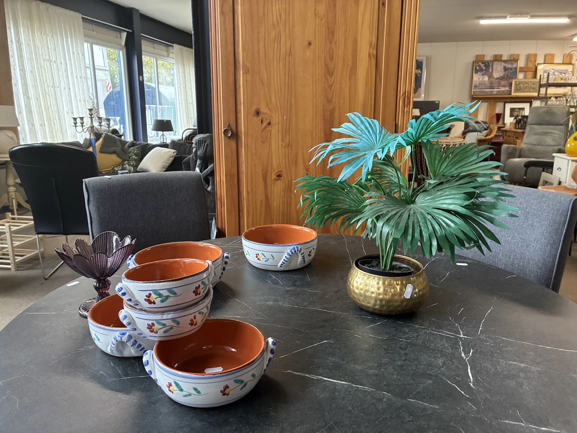 Uitgestalde decoratieve serviesgoed en potplanten op een donkere tafel in de winkel