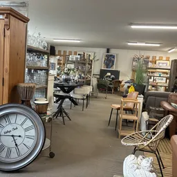 Winkelvloer van kringloopwinkel met meubels, kasten, boeken, decoratie en vintage klok op voorgrond