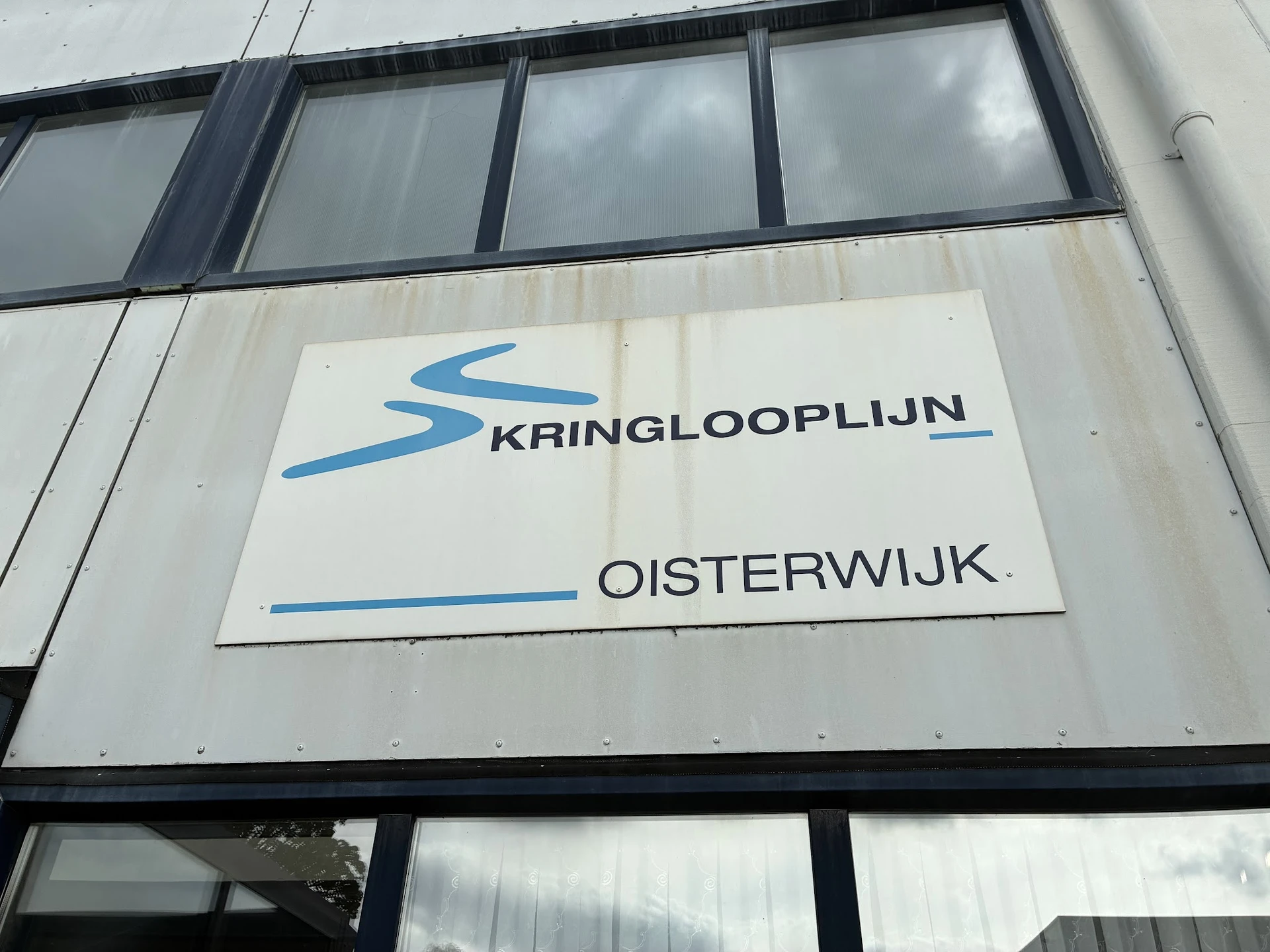 Gevel van kringloopwinkel met wit bord en blauw logo van Kringlooplijn Oisterwijk