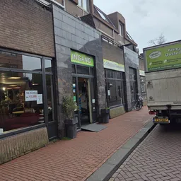 Winkelvoorgevel met groene Kringloop-bord en ingang aan Kanaalstraat, met straat en voorbijrijdende vrachtwagen