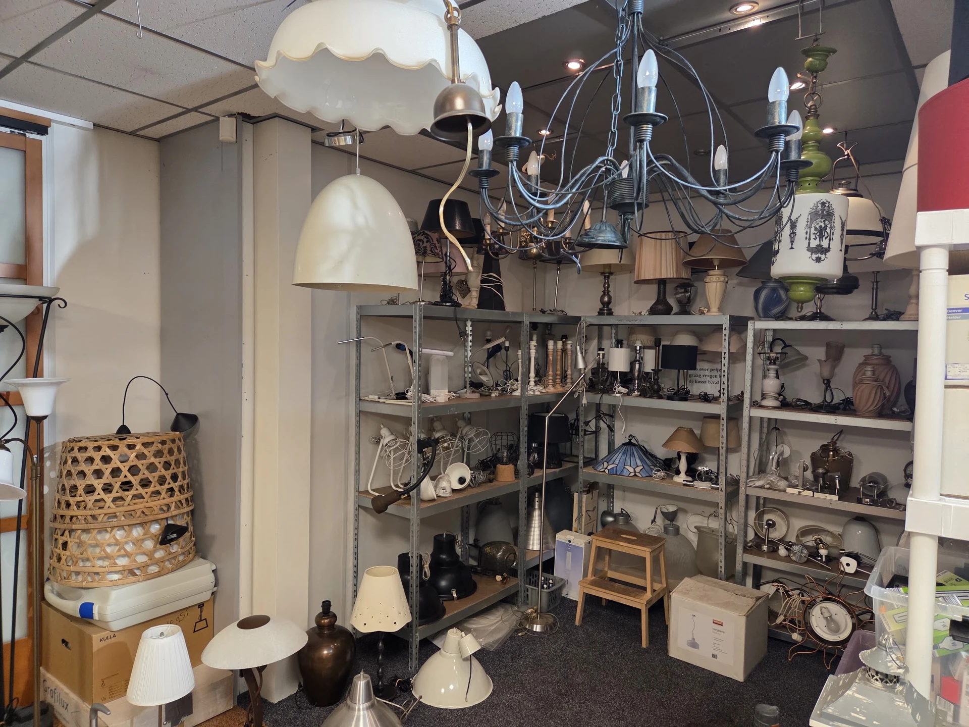 Stellingen vol met tweedehands huishoudelijke artikelen, lampen, kandelaars en decoratieve items